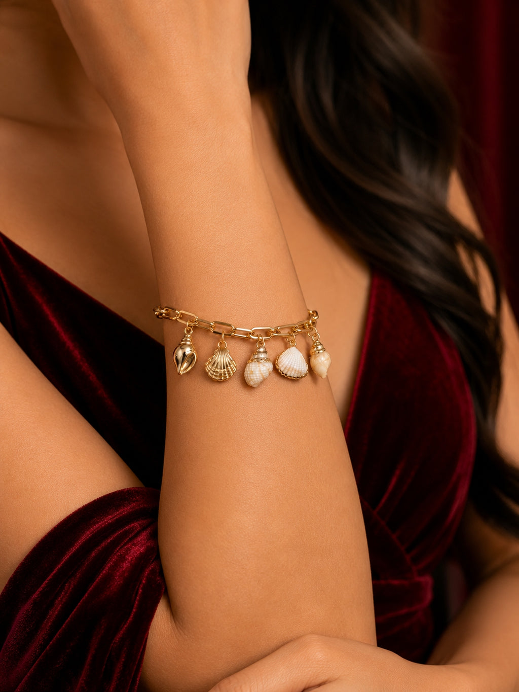 Gold seashell charm bracelet with mixed shell charms on red velvet background