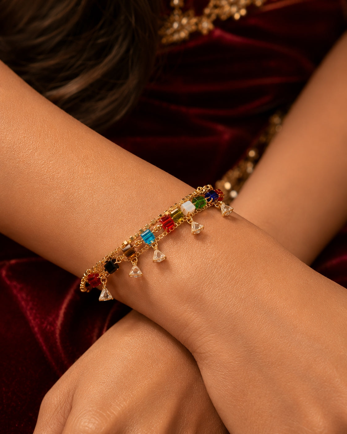 Close-up of multicolour crystal cube and triangle charm bracelet on crossed wrists