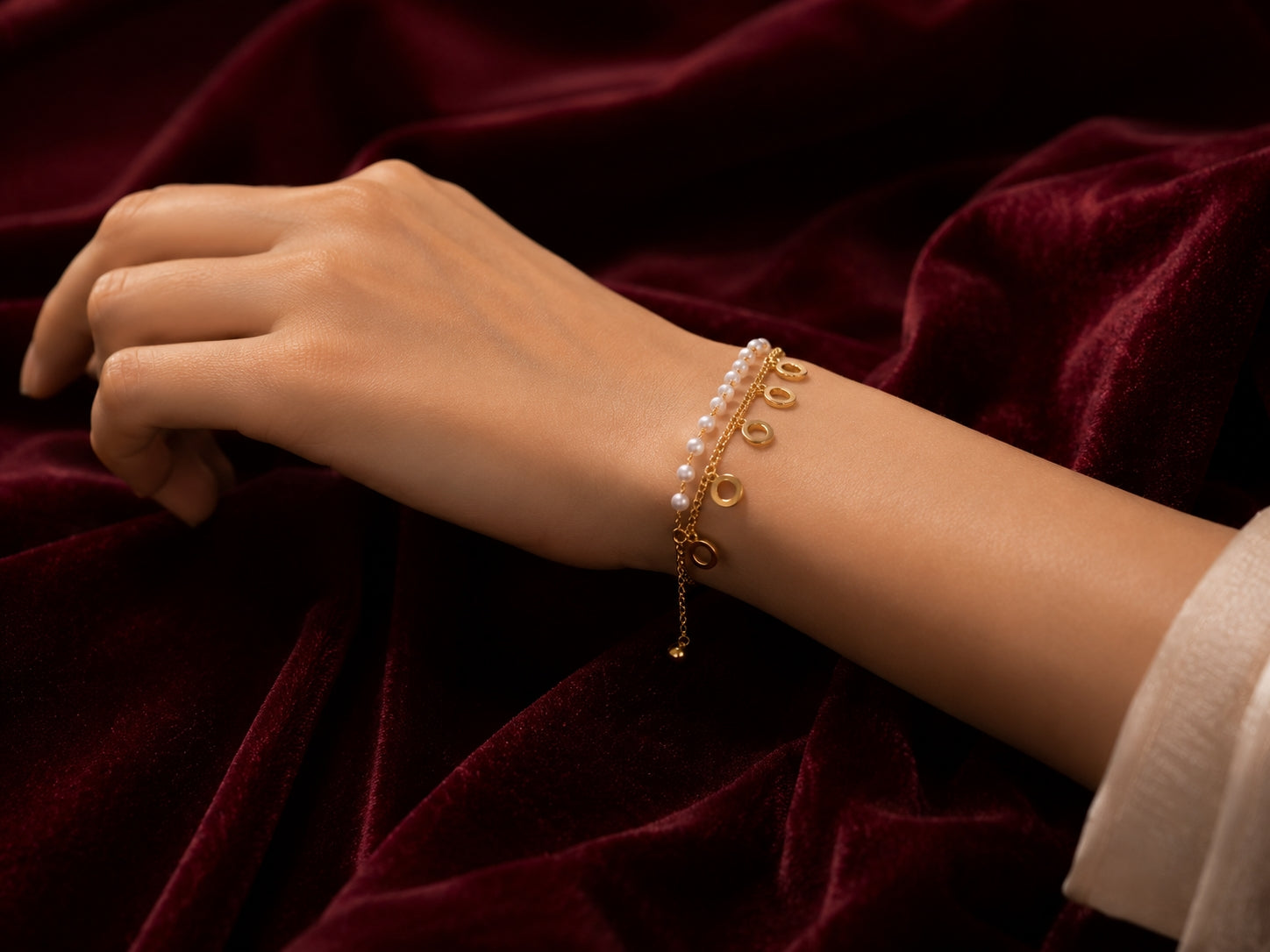 Model wearing gold circle charm bracelet on wrist against burgundy velvet