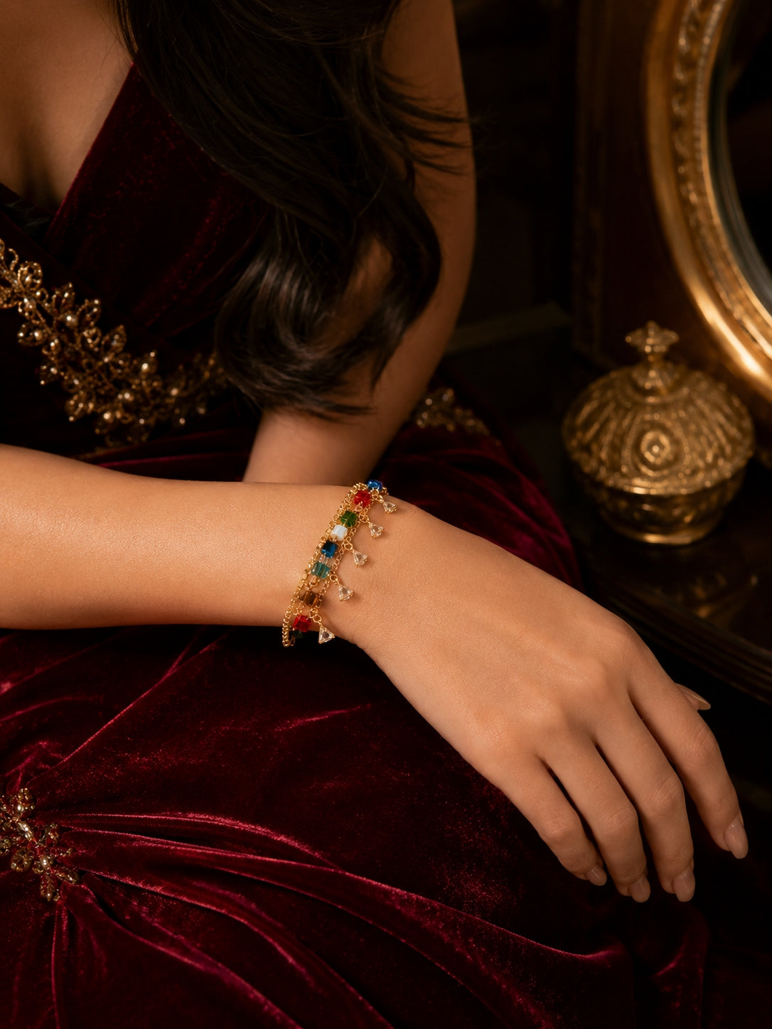 Model wearing gold multicolour crystal cube bracelet on wrist in maroon velvet outfit