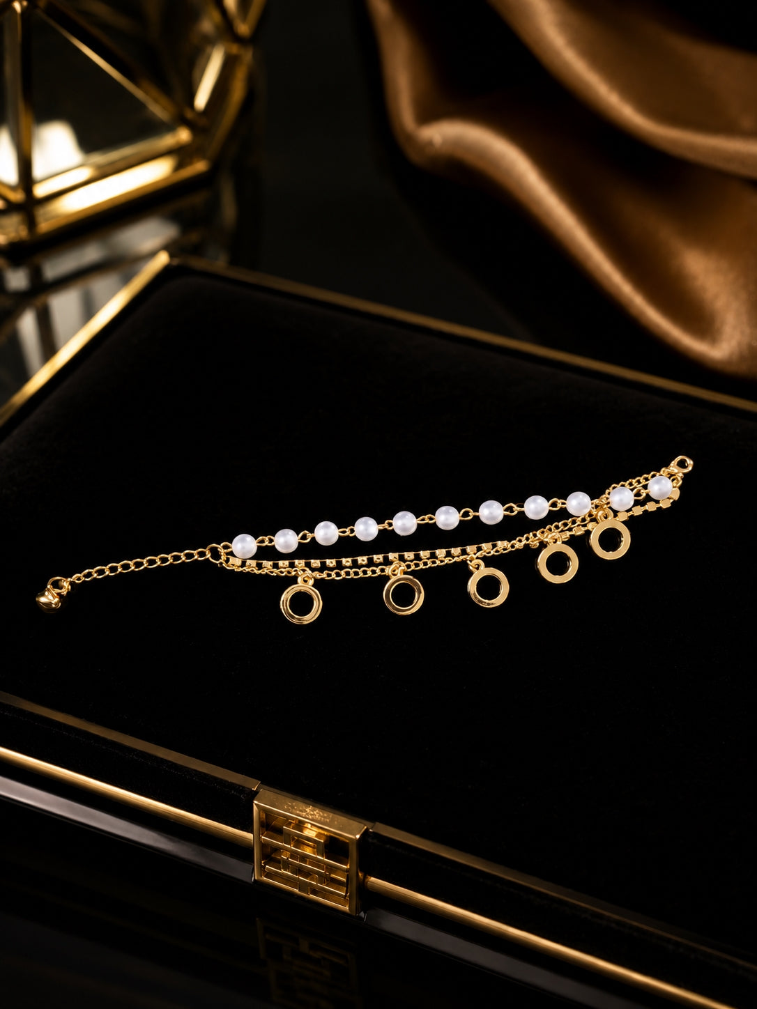 Gold-toned pearl and circle charm layered bracelet on black velvet jewellery box
