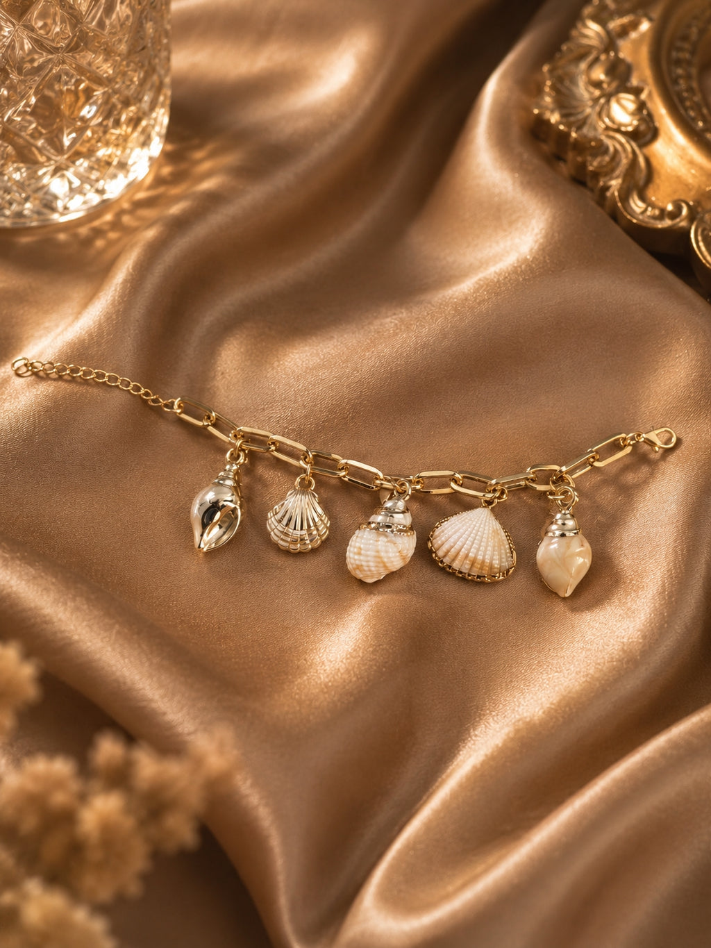 Gold-toned seashell charm bracelet flat lay on gold satin fabric