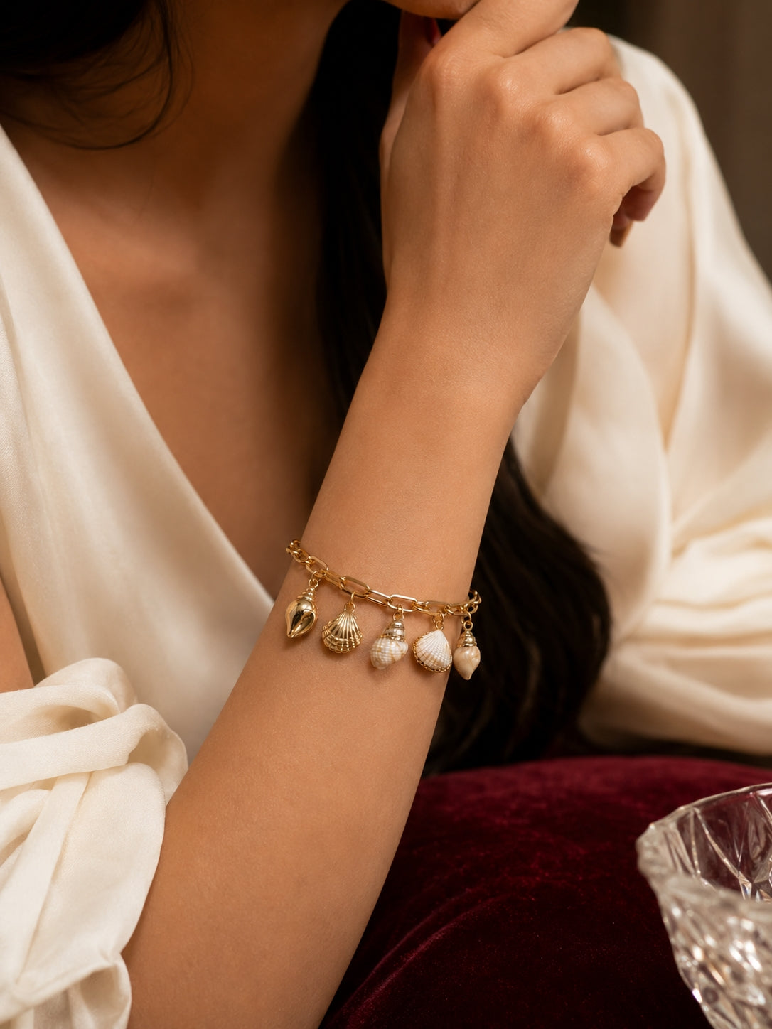 Model wearing trendy gold shell charm bracelet on wrist in white outfit