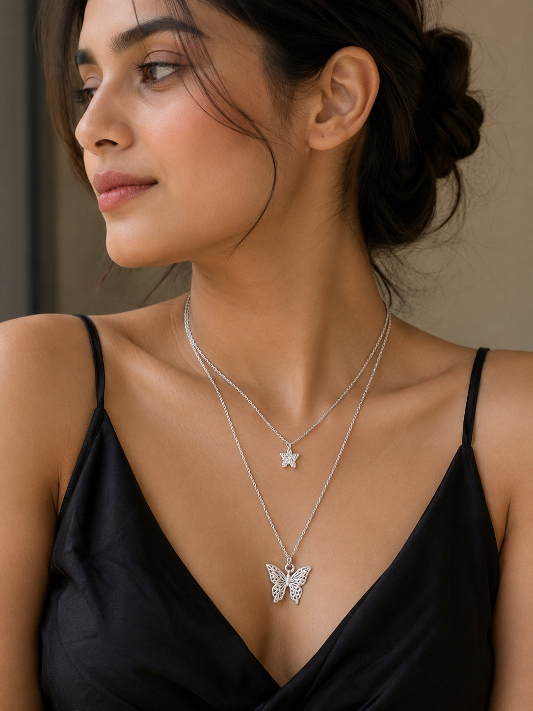 Model wearing silver double-layer butterfly pendant necklace on black top